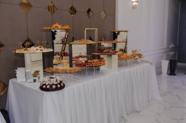 Beyaz çarşaflı lüks bir salonda şık bir açık büfe düzenleme çeşitli aperatifler ve tatlılar, süslü dekorlar ve cilalı mermer döşemeler sergilenmektedir..