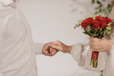 Aşk ve bağlılığı simgeleyen iki insanın el ele tutuştuğu bir düğün seremonisini yakalamak, bir buket canlı kırmızı gülün sahnenin içine romantizm kattığı bir an..