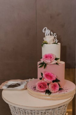 Güzel dekore edilmiş iki katlı pembe bir düğün pastası beyaz ve pembe güllerle süslenmiş ve altın rengi bir 