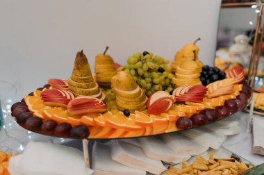 Çok güzel düzenlenmiş bir meyve tabağı servis standında dilimlenmiş portakallar, elmalar, armutlar, üzümler, böğürtlenler ve diğer meyveler rengarenk ve davetkar bir şekilde sergilenir.