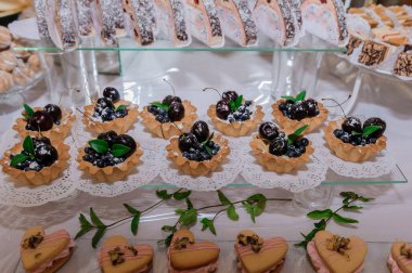 Beyaz bir masa üzerinde güzel dekore edilmiş vişneli turtalar, küçük dörtler ve canoli içeren nefis bir pasta gösterisi..