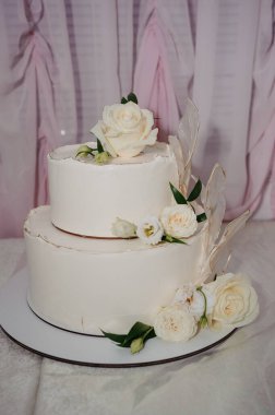 Beyaz Güller ve Masadaki Altın Aksanlı Zarif İki Kademe Düğün Pastası Yumuşak Pembe Örtülü, Aşk ve Romantizmi Kutlayan.