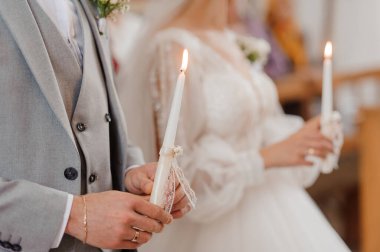Gelin ve damadın birliktelik mumlarını yaktığı romantik bir düğün sahnesi. Çiftin bağlılık yeminlerini sembolize ediyor. Şık resmi kıyafetler, gösterişli dantel ve gri takımlar..
