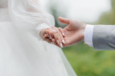 Gelin ve damadın el ele tutuşup evlilik yüzüklerini ve bağlılıklarını sergiledikleri bulanık doğal bahçe arkaplanlarıyla bir düğün töreninde çekilen hassas bir an..