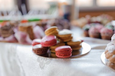 Renkli badem kurabiyelerinin ve pişmiş malların katmanlı servis tabağında sergilenmesi özel bir durum için pastel tonlu davetkar bir tatlı sergilenmesi..