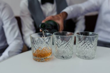 Rafine bir etkinlikte garsonun doldurduğu üç kristal bardakla resmi viski dökme töreni, kutlama ve lüks yakın çekim önerisi.