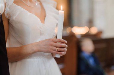 Beyaz fırfırlı elbiseli ışıl ışıl bir gelin, kilise ortamındaki bir düğün töreninde yanan bir mum tutuyor. Bulanık bir geçmişi ve inancı simgeliyor..