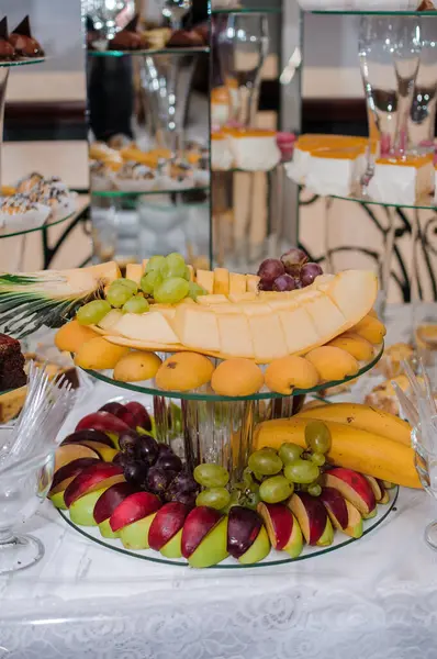 Elmalar, muzlar, üzümler, kavunlar ve pastanın dantelli kumaşla süslendiği kaliteli şampanya flütleri içeren nefis bir düğün tatlı masası..