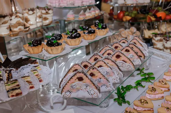 Düğün resepsiyonunda müsrif bir tatlı masası gösterisinde karışık dekore edilmiş çikolatalı turtalar, kirazlı mini meyveli turtalar ve katmanlı sünger kekler yer alıyor.