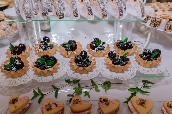 Beyaz bir masa üzerinde güzel dekore edilmiş vişneli turtalar, küçük dörtler ve canoli içeren nefis bir pasta gösterisi..