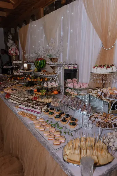 Şeftali Kaplama ve Bol Şekerli Düğün Tatlıları Dekoratif Çiçek Düzenleme ve Misafirlerle Şatafatlı Kutlama Ayarlarıyla Ayrıntılı Bir Düğün Tatlısı Masa Gösterimi.