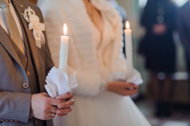 Bir düğün sırasında, damat ve gelinin mumları ve beyaz dantel dokuları tutuşturduğu, kilisenin içindeki birlik ve inancı simgeleyen hassas bir sahne.