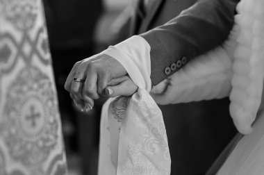 Bir gelin ve damadın ellerinin birleştiği, evlilik yüzüklerine ve kumaş dokularına odaklanmış, aşkı ifade eden tek renkli bir an.