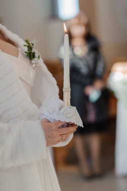 Görüntü, kilisedeki dini bir düğün töreninde elinde yanan, süslü bir mum tutan beyaz bir elbise ve ceket giyen bir geline odaklanıyor.