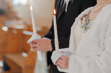 Siyah takım elbiseli bir damat ve beyaz elbiseli ve kürklü bir gelinin yakın plan görüntüsü. Süslü kilisenin içinde yanan mumlar, ışık değişimi.