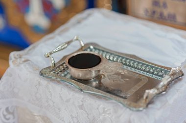 Süslü çiçek detaylarıyla cilalanmış gümüş tepsi içinde kahve bulunan küçük, koyu renkli bir fincanı gösterir. Muhtemelen el değmemiş beyaz bir dantel masa örtüsünün üzerinde durmaktadır.
