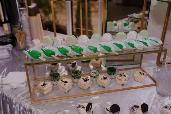 Müsrif bir tatlı düzeneği, altın katlı stantlarda sunulan, nefis kaplarda nefis yeşil ve beyaz badem kurabiyeleri sergiliyor.