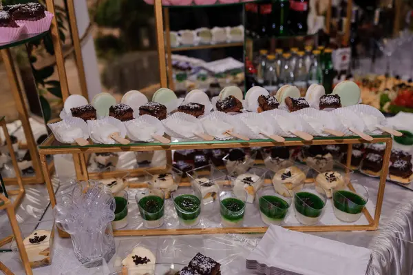 Lüks etkinlik masasında pastel makaronlar, çubuklardaki çikolata kareleri ve süslü altın katlı raflarda sergilenen canlı yeşil parfe de dahil olmak üzere nefis tatlılar sergileniyor.