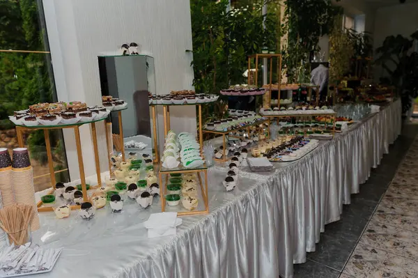 Lüks gümüş bir bezle örtülmüş uzun bir masa etkileyici bir tatlı büfesine ev sahipliği yapıyor. Çoklu katmanlı tezgahlarda çikolatalar, pastalar ve diğer tatlılar sunuluyor.