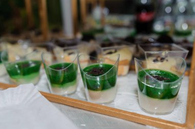 Yemek büfesinde dört yeşil katmanlı tatlı fincanı sergilenen servis tepsisinin yakın çekimi, yemek sunumuna odaklı canlı, zarif bir etkinlik öneriyor.