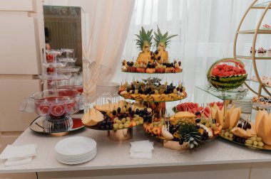 Güzelce hazırlanmış düğün tatlıları arasında bir katmanlı meyve sergisi, karpuz oyma ve şeftali ve beyaz örtüyle şekillendirilmiş cam punç fıskiyesi yer alıyor.