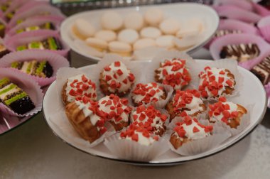 Zarif pembe badem kurabiyelerinin, renkli minyatür keklerin ve zarif gümüş tepsilerde beyaz çikolata kaplı pastaların yer aldığı güzel düzenlenmiş bir tatlı büfesinin yakın çekimi.