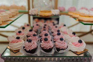 Böğürtlenlerle süslenmiş pembe şekerli kekler ve parıltılı altın katlı pastalar düğün veya kutlama için idealdir.