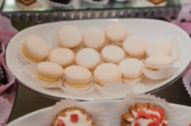 Beyaz bir tabakta soluk pembe badem kurabiyeleri bulunur. Sofistike bir tatlı sergisi ya da kutlama etkinliği için mükemmeldir.