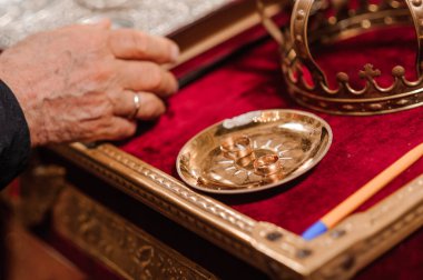 Yakın çekim bir Ortodoks düğün törenini betimliyor, altın bir taç sergileniyor, gümüş tepside alyanslar, ve dini gelenekleri ön plana çıkaran kırmızı kadife bir bez.