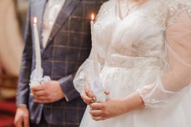 Güzel bir gelin ve damat, kilisenin içinde yanan mumlar tutuyorlar. Resim romantizm, inanç ve bağlılık yayıyor. Düğün temalı projeler için ideal.