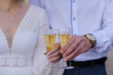 Gelin ve damadın şampanya bardaklarıyla kadeh kaldırdığı, ellerine odaklanan ve şık giyinen yakın çekim romantizm, kutlama ve lüks bir görüntü yayar.