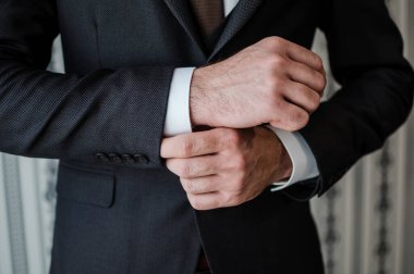 Koyu gri takım elbiseli bir adamın, beyaz kol düğmelerini ayarlarken, profesyonel iş kıyafetini ve sofistikeliğini temsil ederken çekilmiş yakın plan bir fotoğrafı.