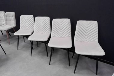 Dört sıra soluk pembe kadife yemek sandalyesi, kendine özgü yorganlı sırtları ve parlak siyah metal bacakları, modern ev dekorasyonu için ideal koyu gri bir zeminde sergileniyor.