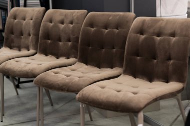 Modern bir sergi salonunda dört kahverengi kadife yemek sandalyesi sergileniyor. Metal bacaklar ve minimalist bir ortam, lüks ev mobilyaları olduğunu gösteriyor.
