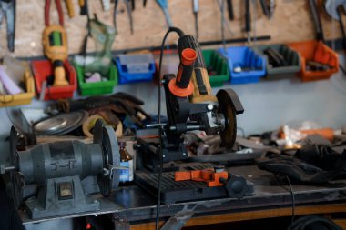 Düzensiz bir atölye sahnesinde iki metal öğütücü bir tezgah üzerinde, plastik kutularda aletler ve bir deri iş eldiveni ile çevrili, metal bir çalışma ortamı tasvir ediliyor.