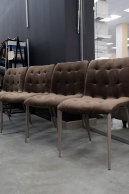 Metalik bacaklı dört kahverengi kadife yemek sandalyesi ve parlak, minimalist bir stüdyo alanına yerleştirilmiş düğmeli sırtlar aynada yansıyor.