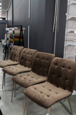 Düğme düğmeli ve parlak metal bacaklı dört adet modern kahverengi kadife yemek sandalyesi, kumaş örnekleriyle minimalist bir sergi salonunda sergileniyor..