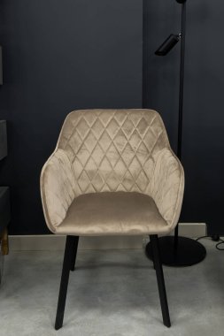 Karmaşık bej kadife bir yemek sandalyesi. Elmas kaplamalı bir sırt sehpası var. Koyu gri bir duvara karşı duruyor.