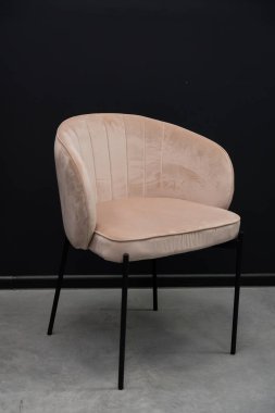 Dikey kanal aksanlı şık pembe kadife bir sandalye, açık gri beton zeminde, koyu bir zemin üzerinde oturur, yemek ve yaşam alanları için modern, minimalist bir oturma çözümü sunar.