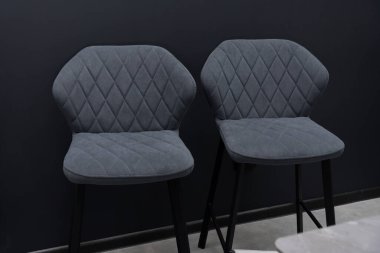 Elmas yorgan ve siyah metal bacaklı iki parlak, koyu gri kadife yemek sandalyesi, çağdaş ev mobilyalarını temsil eden karanlık bir duvara karşı sergileniyor.