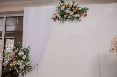 Güzel dekore edilmiş bir düğün arka planında pembe, beyaz ve yeşil çiçeklerle süslenmiş çiçeklerle romantik bir tören için beyaz kumaş zemin oluşturulur.