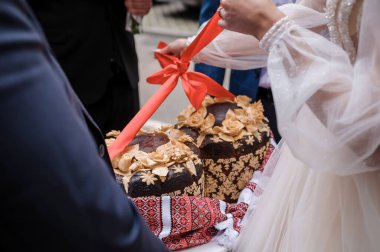 Bu iç açıcı görüntü bir Bulgar düğün ritüelini tasvir ediyor: Poga adında tatlı bir ekmek kesen bir çift, kırmızı kurdele ve karmaşık ayrıntılarla süslenmiş, refahı simgeliyor