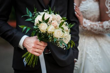 Bir damat güzel bir buket fildişi gül ve bebek nefesi tutar. Yanında gelini, resmi bir düğün kutlaması sunar. Ayrıntılı dantel bir elbiseyle.