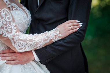 Yakın plan çekimde yeni evli bir çift birbirine sarılıyor, alyanslarına ve gelinin elbisesinin karmaşık danteline odaklanıyor, aşkı ve bağlılığı tasvir ediyor.