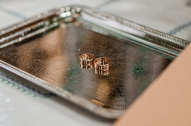 Yakın plan çekimde iki altın alyans süslenmiş gümüş tepside duruyor. Aşkı, bağlılığı ve lüks bir düğün kutlamasını sembolize ediyor.