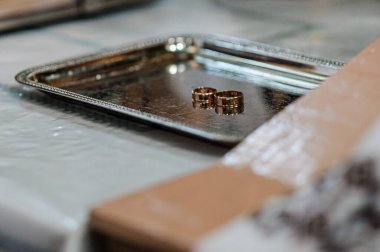 İki altın alyansın yakın plan görüntüsü süslü gümüş bir tepside duruyor. Romantik bir birlikteliği, bağlılığı ve evlilik kutlamasını temsil ediyor.