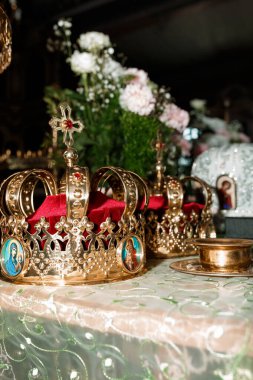 Güzel düzenlenmiş bir sahne, kırmızı kadife ile süslenmiş altın Ortodoks düğün tacını, bereketli bir çiçek aranjmanı ve kutsal dini simgeleri resmediyor.
