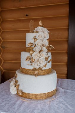 Altın kurdele ve narin güllerle süslenmiş çarpıcı beyaz bir düğün pastası romantik ve lüks bir tatlıyı gözler önüne seren ahşap bir arka planda güzel duruyor.