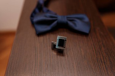 Koyu mavi bir papyon ve gümüş yakalı bir rozet içeren yakın plan bir resim zengin, koyu kahverengi ahşap bir masa üzerinde dinleniyor, sofistike resmi nikah kıyafeti sergileniyor.