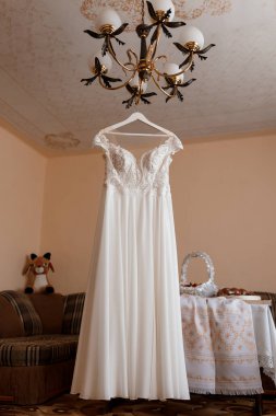 Güzel bir fildişi gelinlik zarif bir şekilde dekore edilmiş klasik avizesi, yumuşak ışıklandırması ve sıcak, romantik bir havası olan eski bir odada asılı duruyor.